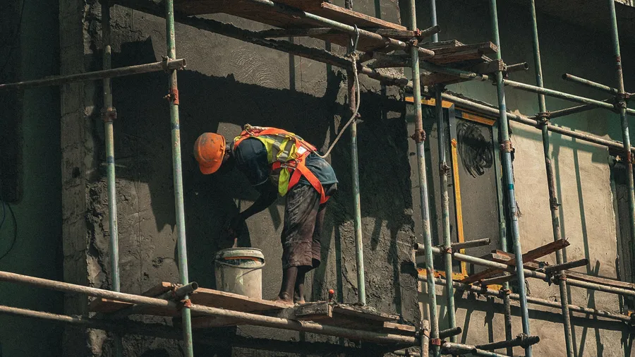 A worker in a hi-vis vest on scaffolding inside a concrete building under construction.
