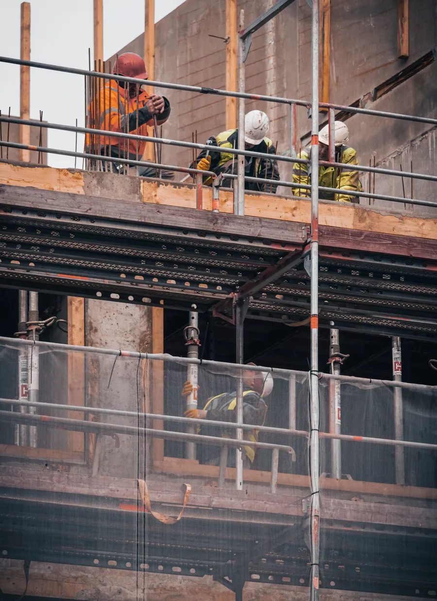 Construction workers on scaffolding against a brick building facade.