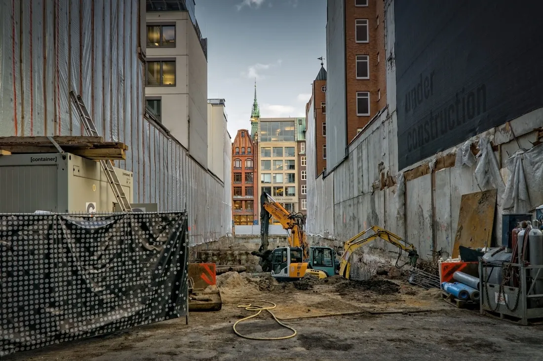 An urban construction site enclosed by hoarding, city buildings rising behind it.