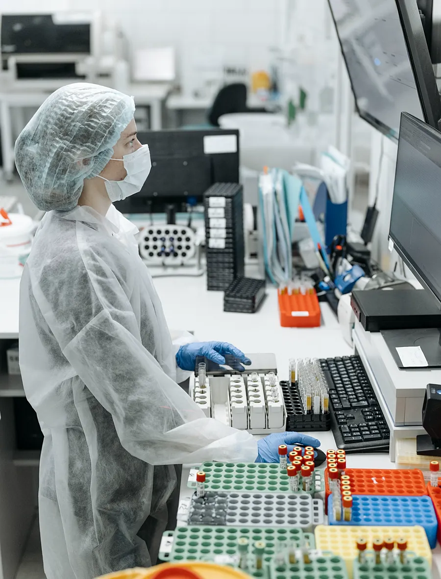 A technician in full cleanroom coverall at a controlled-environment workstation.